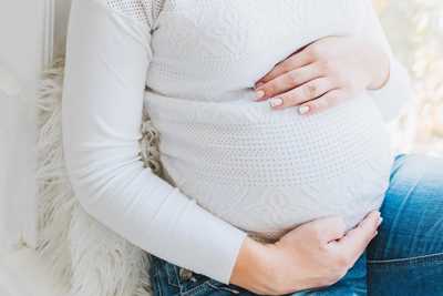 Pregnant woman in white shirt holding stomach